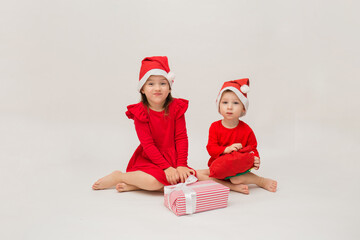 Obraz premium little brother and sister in Christmas costumes with caps with gifts on a white background