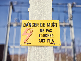 Yellow electric hazard sign near railroad. Danger of death warning in French.