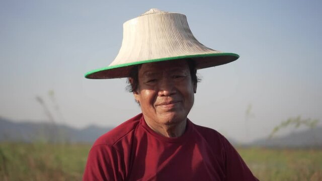 Close up portrait of an asian male fisherman's face Wearing a hat sitting on a fishing boat in blurry natural background. old man looking at the camera . Slow motion hand held Shot 