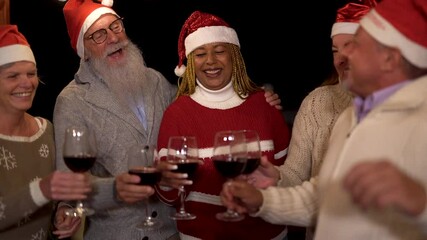 Happy multiracial senior friends celebrate christmas together while cheering with red wine at home on patio