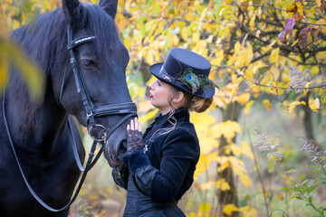 Beautiful girl in vintage clothes and a black horse on an autumn day.