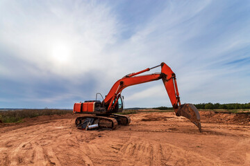 Red excavator on a construction site against blue sky.