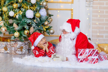 Obraz premium child and Santa Claus near the Christmas tree, boy looks at Santa Claus