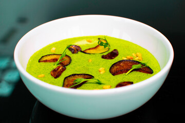Close-up of cream spinach green soup with dried fruits and peanuts in a deep plate