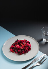 Vinaigrette salad of beetroot, potatoes, beans and carrots served on a white plate on a black and blue background. Natural vegetarian detox snack. Traditional Russian and Ukrainian cuisine