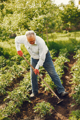 Senior gardener is enjoying his work in garden. Old man in a white shirt. Grandfather with granddaughter.