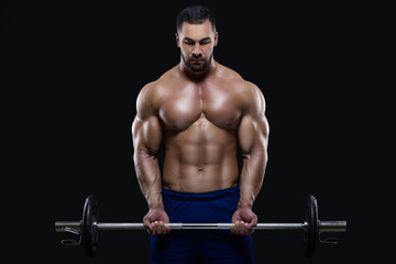Fototapeta na wymiar Handsome fitness man is standing with a heavy barbell ready to workout isolated on black background