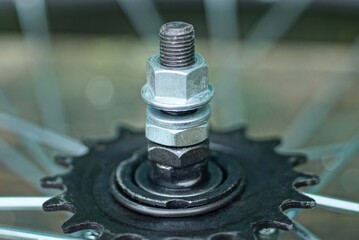 part of a bicycle made of black iron sprocket on a wheel with a bolt and gray nuts