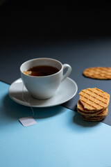 Black tea in a white cup and cookies on a blue and black background. Minimalistic breakfast