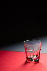 Empty whiskey glass on red and black background. Close-up. Vertical. Copy space