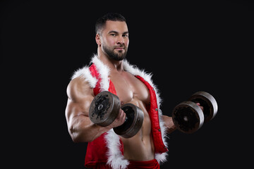 Fototapeta na wymiar Strong muscular athlete wearing Santa Claus costume over naked body is lifting dumbbells isolated on black background