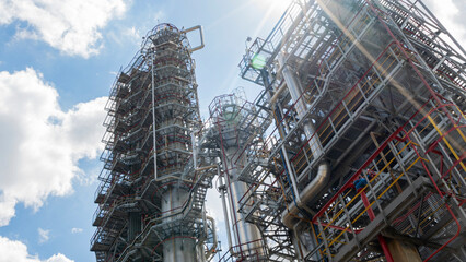 Obraz premium Distillation tower or column on blue sky with clouds background. Oil refinery plant. Refining complex. Petrochemical industry concept.