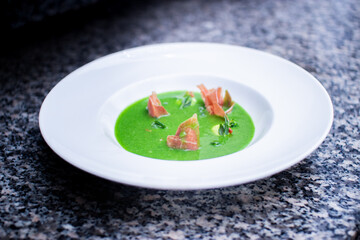 closeup of cream spinach soup with bacon on gray marble on a white plate