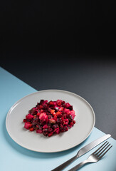 Vinaigrette salad of beetroot, potatoes, beans and carrots served on a white plate on a black and blue background. Natural vegetarian detox snack. Traditional Russian and Ukrainian cuisine