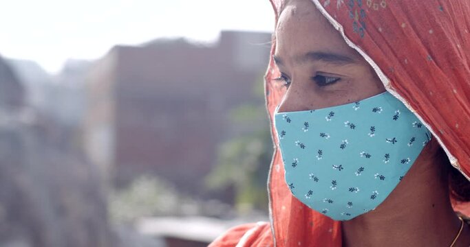 Young Indian adult woman in traditional clothes wearing a face mask for protection from pollution and viruses outdoors communicating with her friends and family using video calling on smart phone 