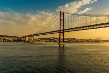 Fototapeta na wymiar On the river Tagus approaching the 25th of April bridge in Lisbon, Portugal in the golden early morning light at sunrise in Autumn