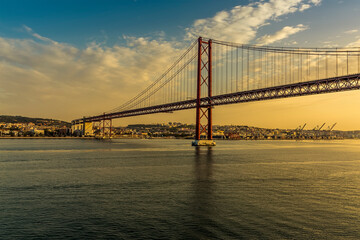Obraz premium On the river Tagus approaching the 25th of April bridge in Lisbon, Portugal in the golden early morning light at sunrise in Autumn