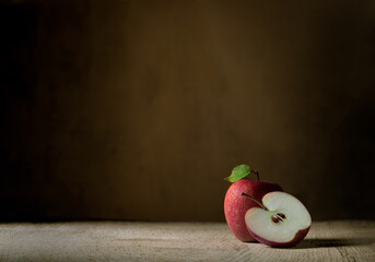 Baseplate with large copy space of one whole and a half red apple, set on a rough wooden board against a dark brown background with directional light from the side and a green leaf on the whole apple