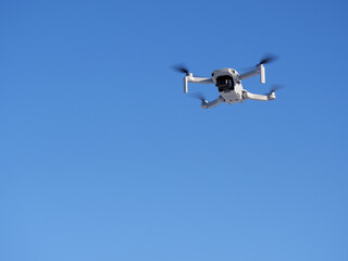 A white quadcopter shoots video in the blue sky. Part of the image is blurred.