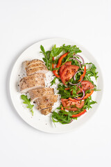 Baked chicken breast with vegetable salad. Chicken fillet with arugula, tomatoes and red bell pepper. White background, top view, copy space