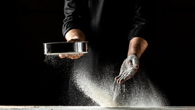 Close-up of male baker kneading the dough, Cook hands kneading dough, sprinkling piece of dough with white wheat flour. On a dark background. Design text placement