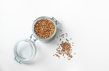 Healthy and gluten free buckwheat in a glass jar and buckwheat grains scattered on the white table, top view