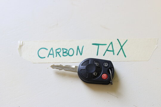 A car key next to a note that says carbon tax. concept of increasing cost to drive or the problems with a carbon tax.