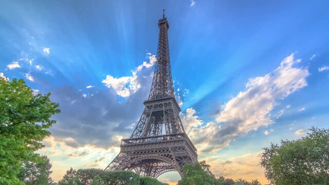 The Eiffel tower with warm rays of light in clouds during sunset timelapse hyperlapse. It is one of the most recognizable landmarks in the world. Blue cloudy sky at sunny evening