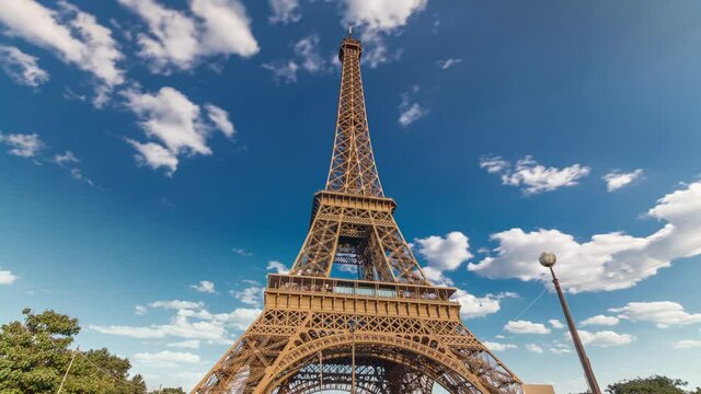 The Eiffel tower with warm light during sunset timelapse hyperlapse. Blue cloudy sky at sunny evening. It is one of the most recognizable landmarks in the world.