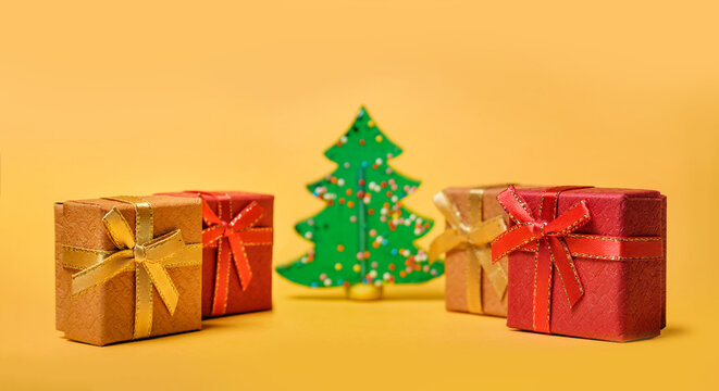 Christmas composition with selective focus. Gift boxes and Christmas tree on a yellow background with copy space.