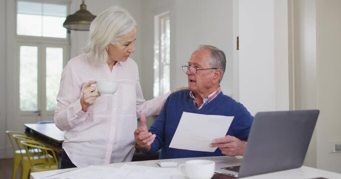 Senior couple with coffee cup using laptop and checking finances at home