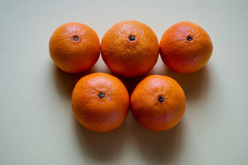 Five unpeeled clementines on a plain background