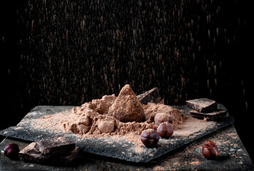 Fototapeta premium Chocolate truffle sprinkled with cacao and golden powder against the black background 