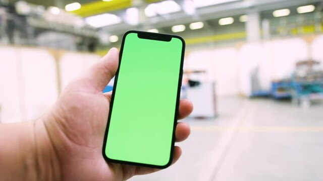 Engineer using Smartphone in Industrial plant with green screen. Greenscreen smart phone holding in bright industry building background. Iot app 
