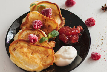 Breakfast with pancakes on plates, sour cream and pavidl. Pancakes are on a white table and the guy is holding in his hands.