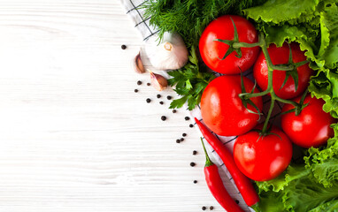 Fresh tomatoes, hot red peppers, garlic and greens lie on the white wooden table. Healthy food concept. Flat lay. Top view. Close-up. Space for text.