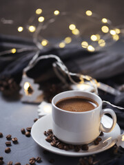 Home holiday comfort, white Cup of freshly brewed espresso coffee, scattered coffee beans, bokeh garland, warm scarf