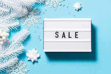 Text Sale on the lightbox on light blue background with white Christmas decorations. Christmas and New Year festive sale concept.