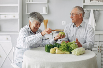 Couple in a kitchen. Grandparents sitting at home. Woman with vegetables