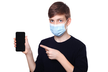 Teen boy in medical protective mask and dark sweater holding mobile phone and pointing on it, isolated on white background.