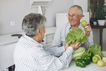 Couple in a kitchen. Grandparents sitting at home. Woman with vegetables