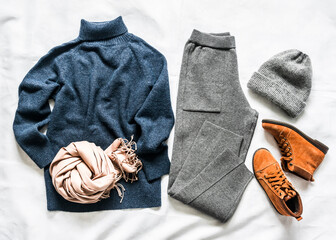 Women's clothing set autumn winter - cashmere blue sweater, knitted sporty pants, suede brown boots, scarf, grey hat on a light background, top view