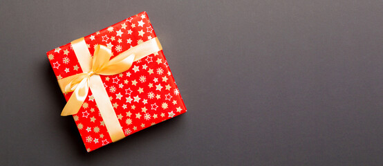 wrapped Christmas or other holiday handmade present in paper with Gold ribbon on black background. Present box, decoration of gift on colored table, top view with copy space