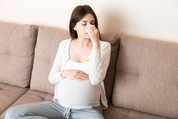 Sick pregnant woman blowing nose into tissue at home Healthy millennial healthcare concept