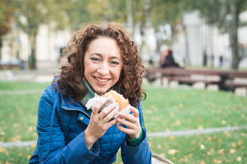 Girl student in a blue jacket eats a hamburger or cheeseburger on the street