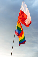 Polska oraz tęczowa flaga z barwami LGBT na tle niebieskiego nieba z białymi chmurami © Mikołaj Rychter