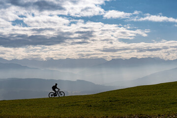 Woman as silhouette riding her electric mountain bike in the Allgaeu alps near Oberstaufen with awesome view into the Bregenz Wald Mountains, Vorarlberg , Austria