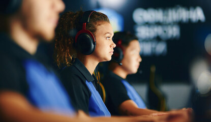 Side view of a focused mixed race girl, female cybersport gamer wearing headphones playing online video games, participating in eSport tournament