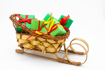 Old-fashioned wicker Santa sleigh with Christmas gifts wrapped in green paper with red ribbon