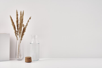 A transparent vase with spikelets and a bottle of water with a cork stopper on a white background....